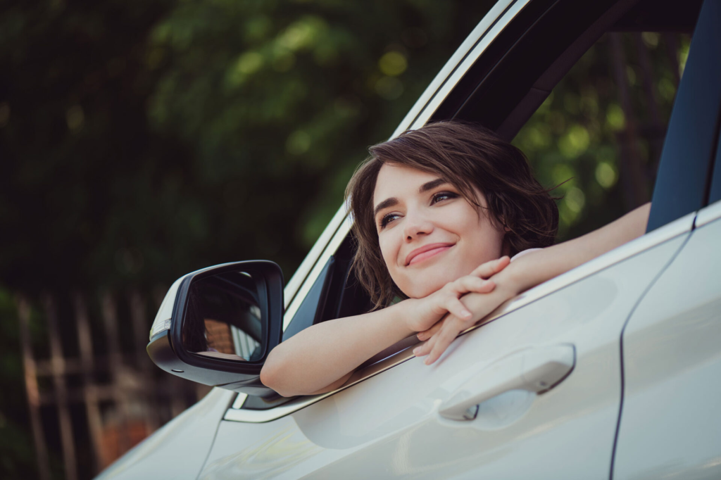 A woman looking outside the window of a car with a smile on her face. "Happy to be starting a new journey"