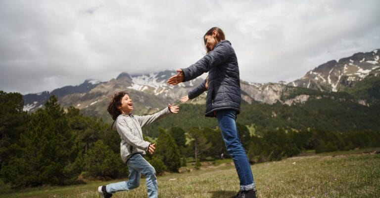 A mother and child embrace joyfully in a lush mountain setting, capturing a moment of happiness and love.