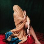 An artistic portrait of a model draped in vibrant fabrics and metallic jewelry, evoking a sense of mystery and elegance.